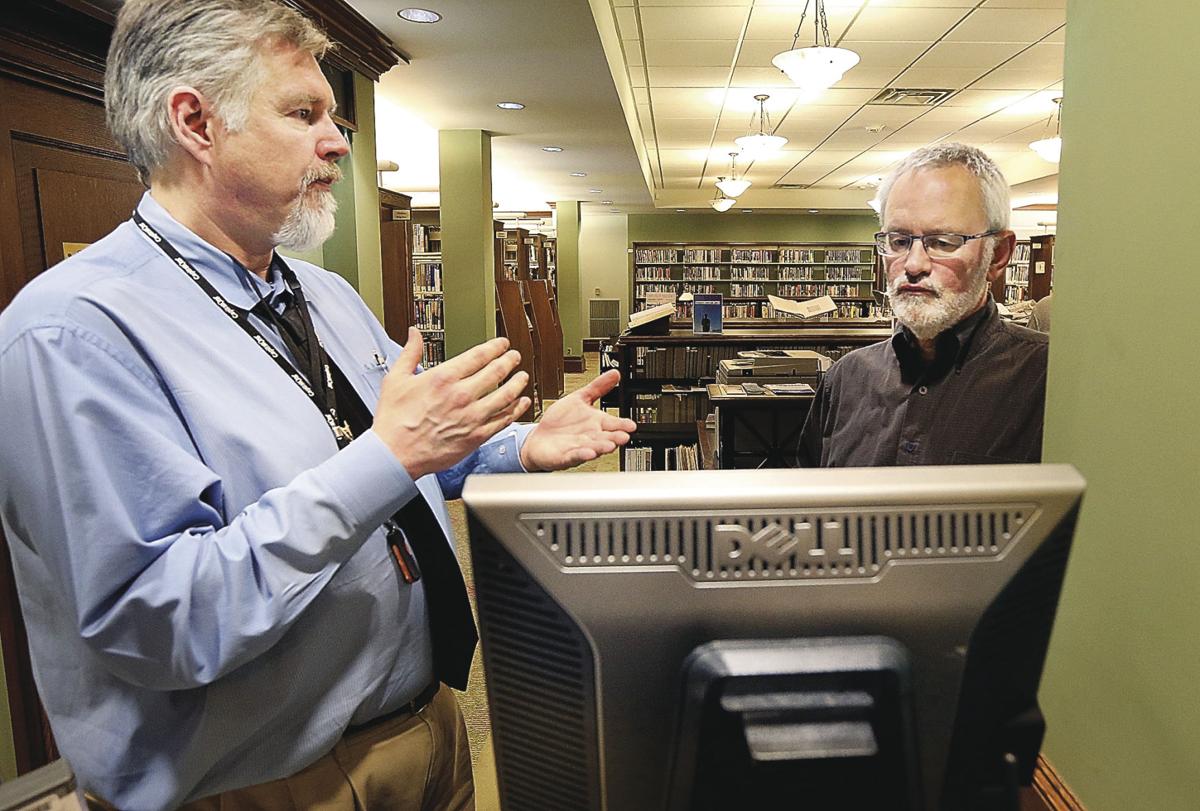 Library worker standing next to and explaining the use of catalog computer to patron