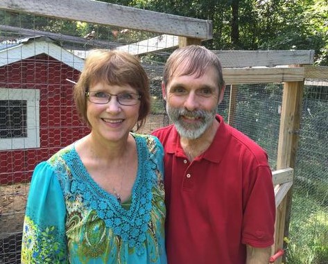 Bruce stands with his wife in front of a chicken coop