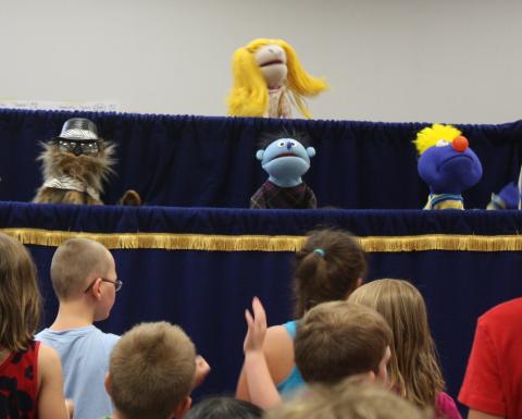 Puppets performing with children dancing in front of stage