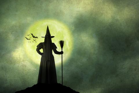 the silhouette of a witch wearing a pointy hat and holding a broom set against a full moon