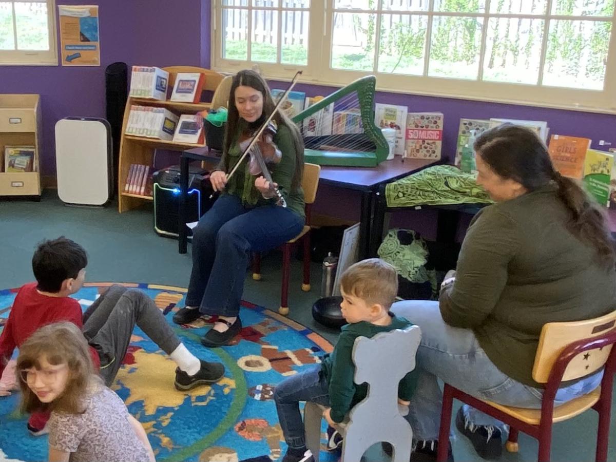 Woman playing fiddle in front of a group of children